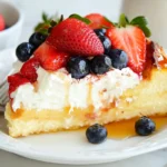 A slice of brioche French toast casserole topped with whipped cream, fresh strawberries, blueberries, and a drizzle of syrup.