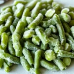 Frozen green beans coated with ice crystals, displayed on a white plate.