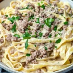 Ground Beef Alfredo pasta garnished with parsley and Parmesan cheese, served in a white bowl